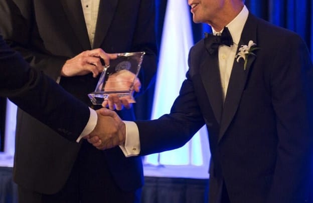 A close-up on the hands of someone presenting an award to another person, who is shaking the hands of a third person