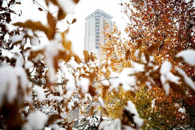 Modern bell tower viewed through autumn leaves covered in snow