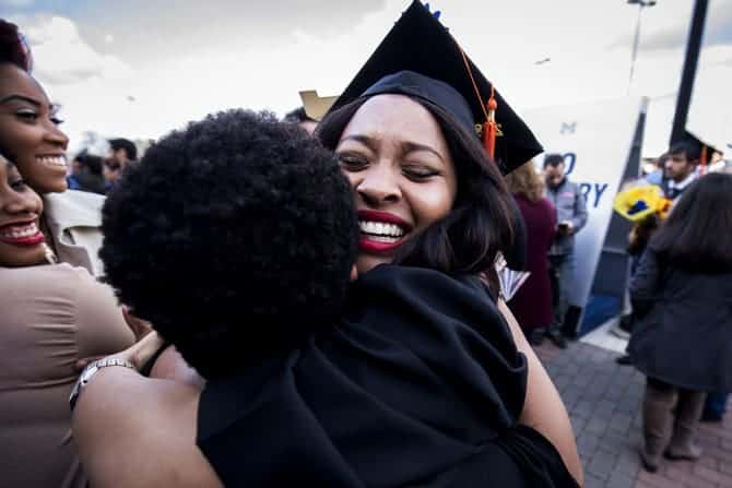 Two people embrace, and one of them wears a graduation cap and robe