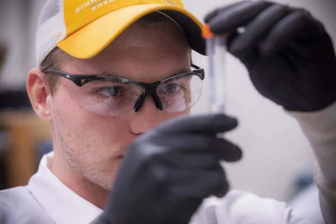 A student handles water samples while wearing safetly goggles and rubber gloves