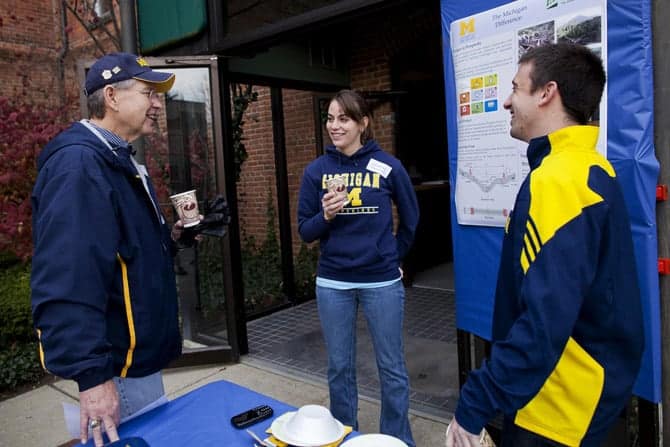 Three people wearing Michigan apparel gather outside a North Campus building
