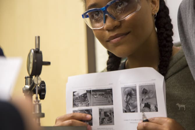 A student wearing safety goggles holds up a packet of paper during a lab class