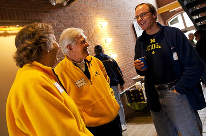 Three people wearing Michigan sweatshirts stand and laugh during an alumni event