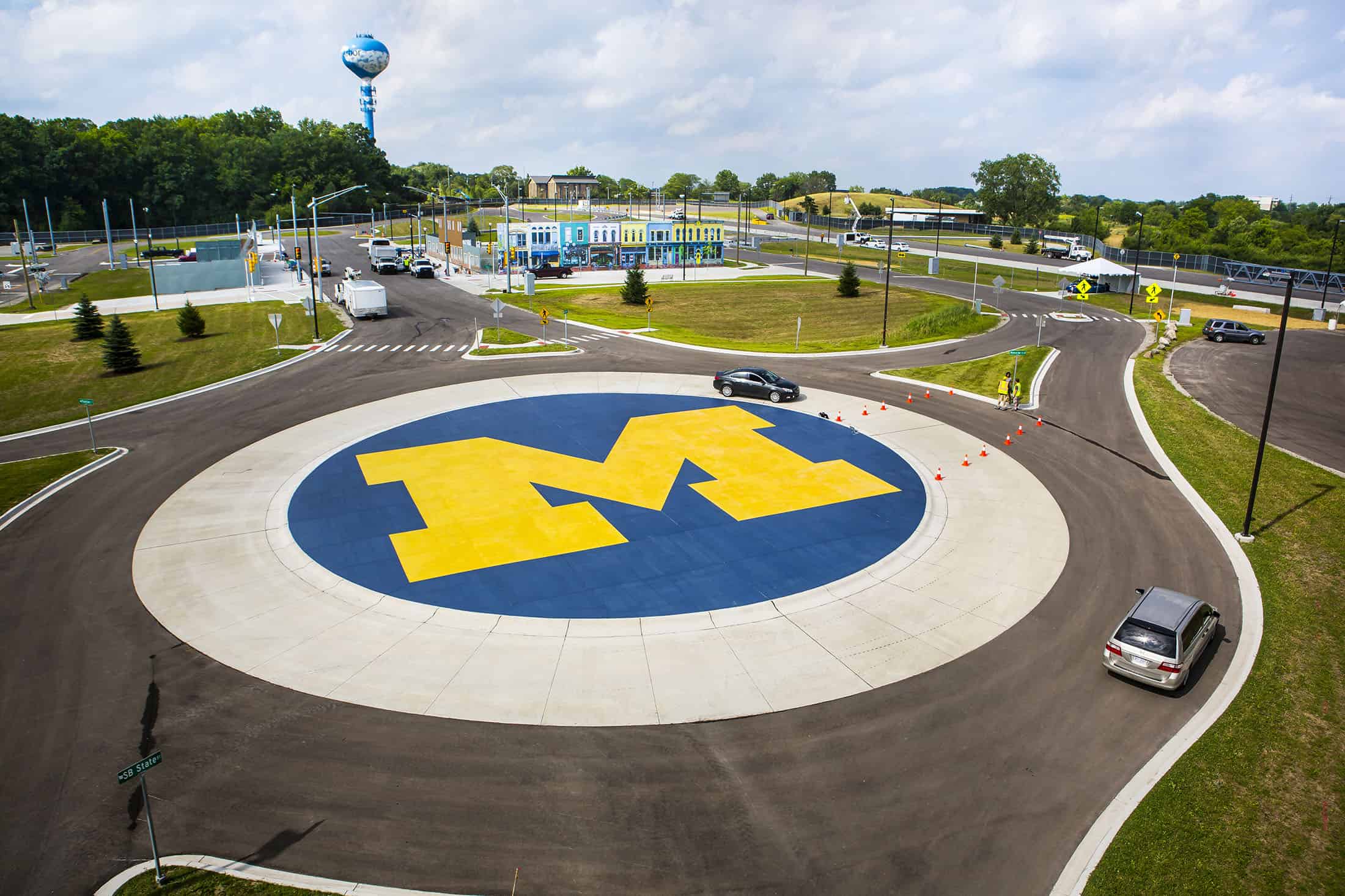 Cars drive around a roundabout with a block M in the middle at the Mcity test facility