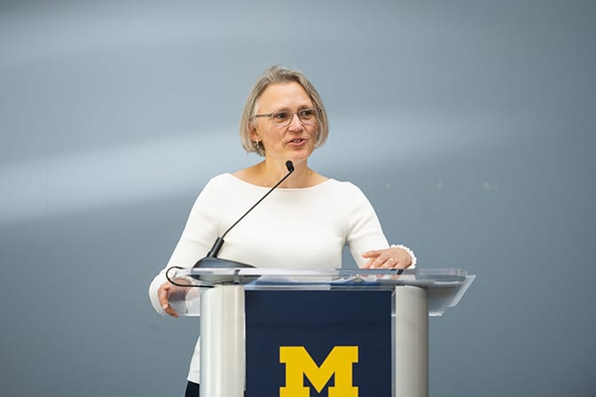 Woman stands at a podium with a University of Michigan logo on it