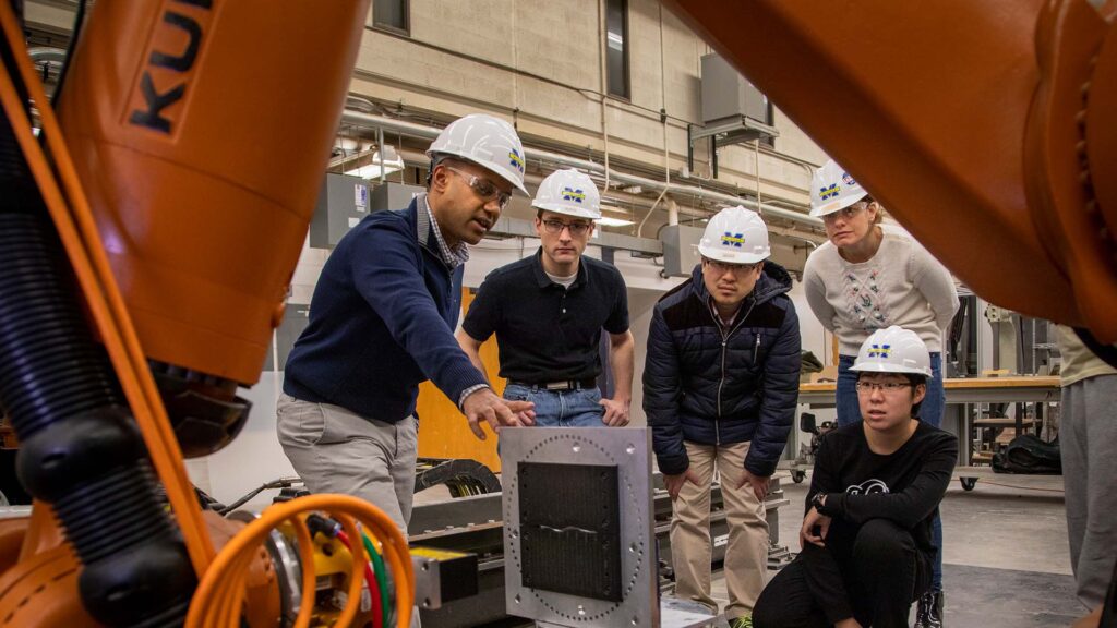 Students and faculty examine robot arm caulking project